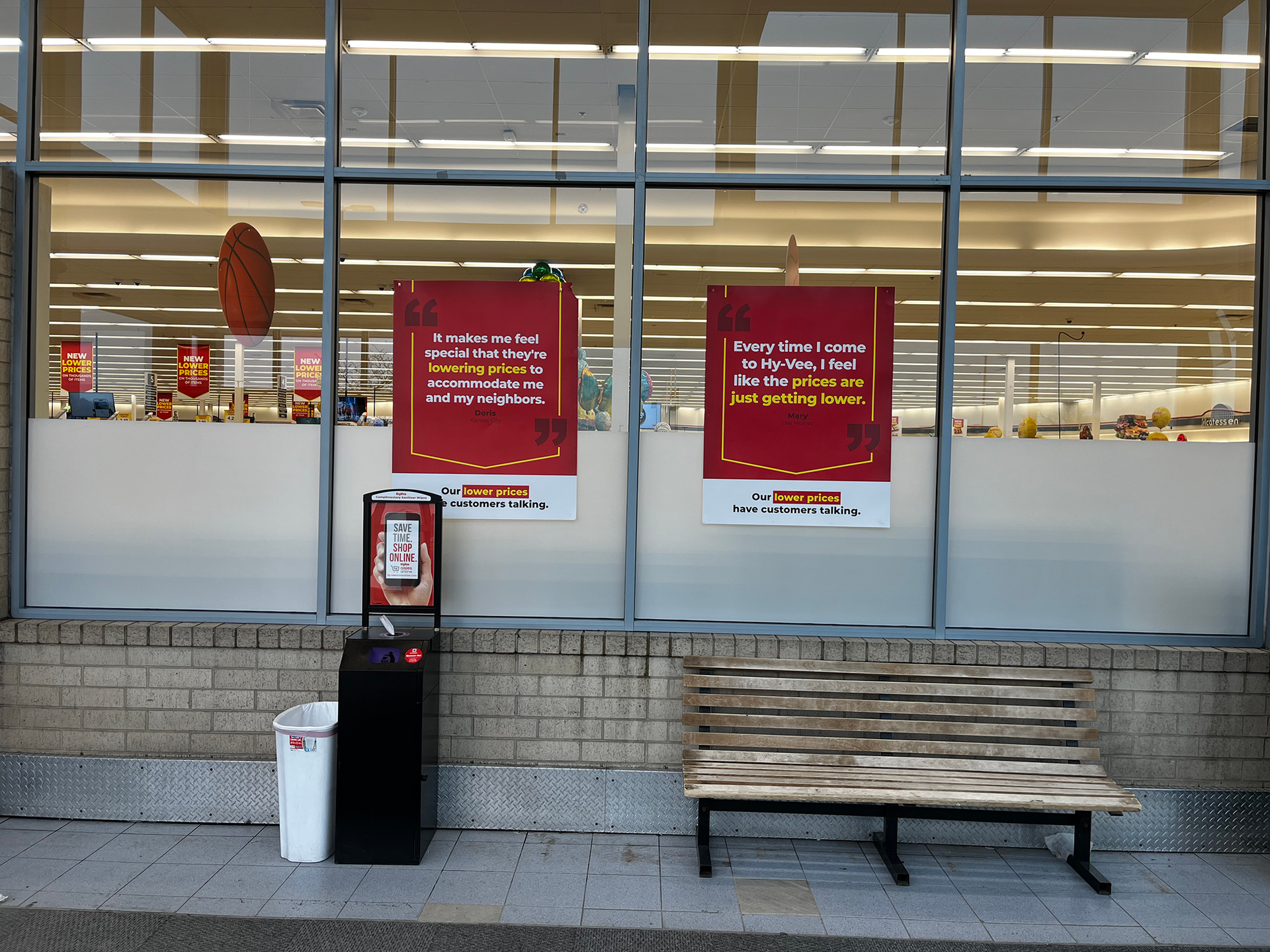 Storefront with two red sale signs, a trash can, and a bench outside large windows