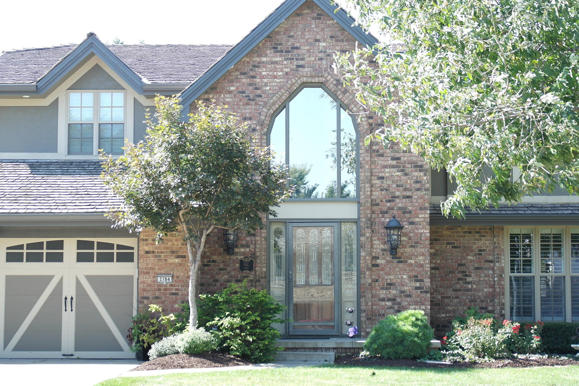 Brick suburban house with a tall arched entry, garage, and trees in front
