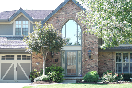 Brick suburban house with a tall arched entry, garage, and trees in front