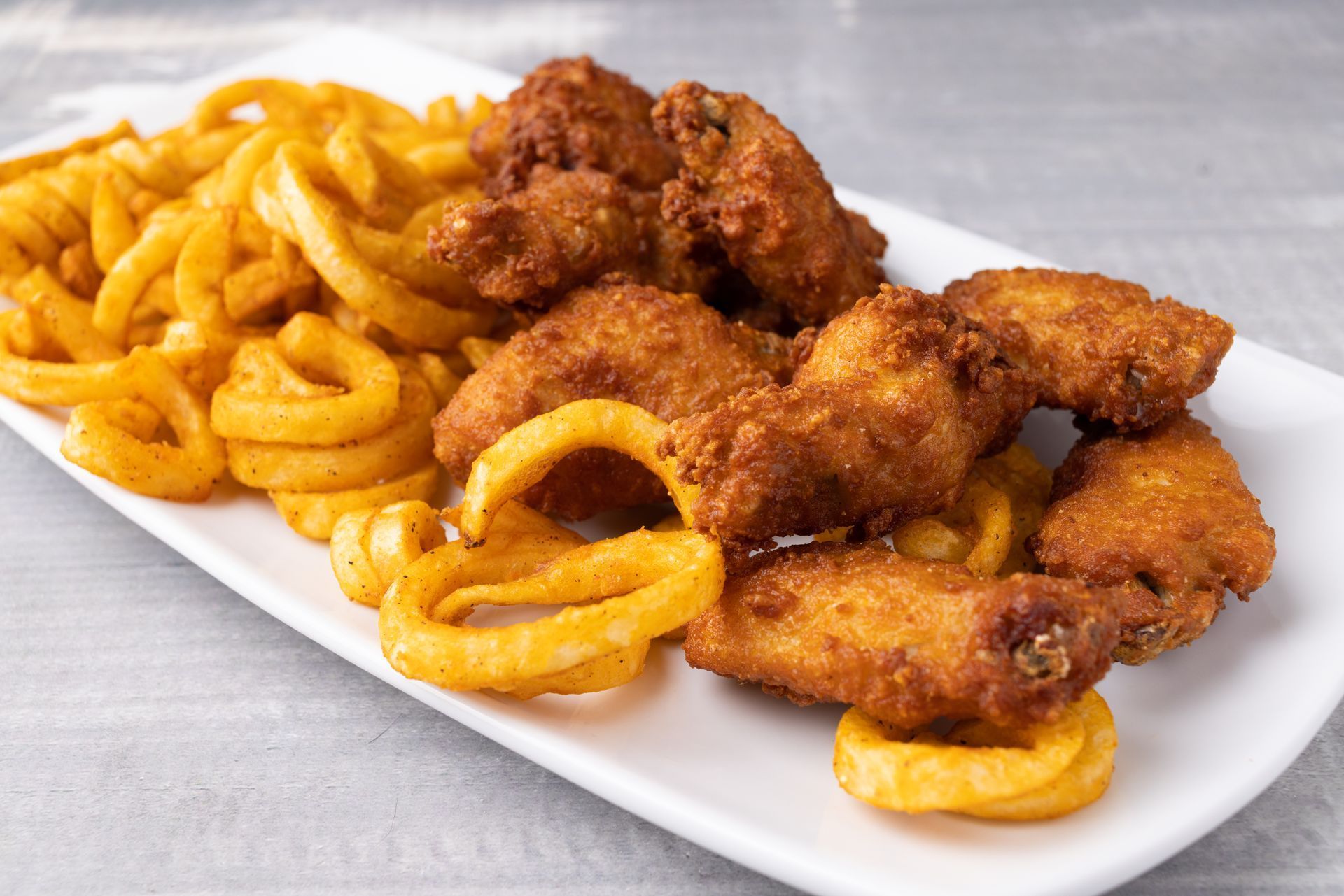 A white plate topped with fried chicken wings and curly fries.