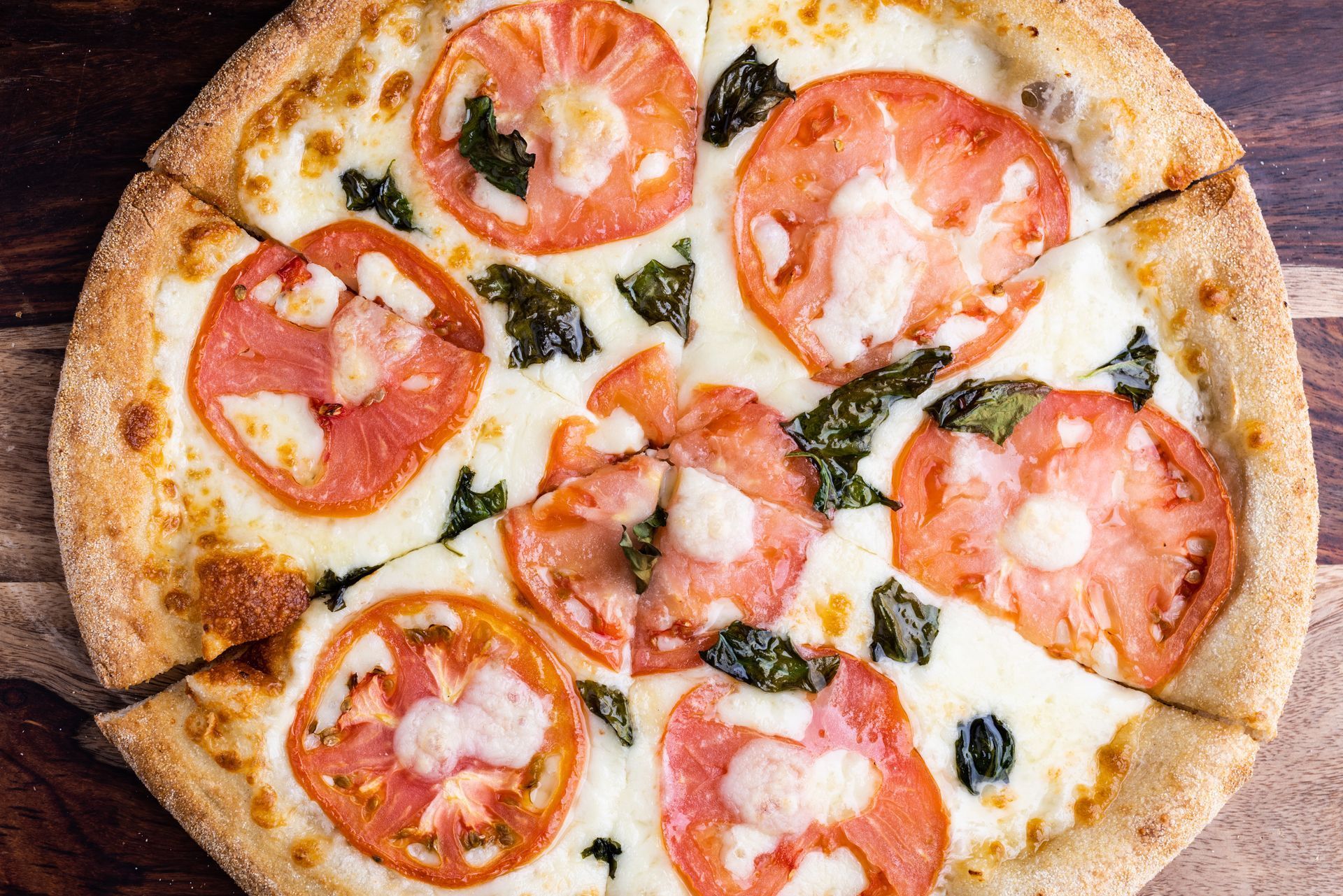 A pizza with tomatoes , cheese and basil on a wooden table.