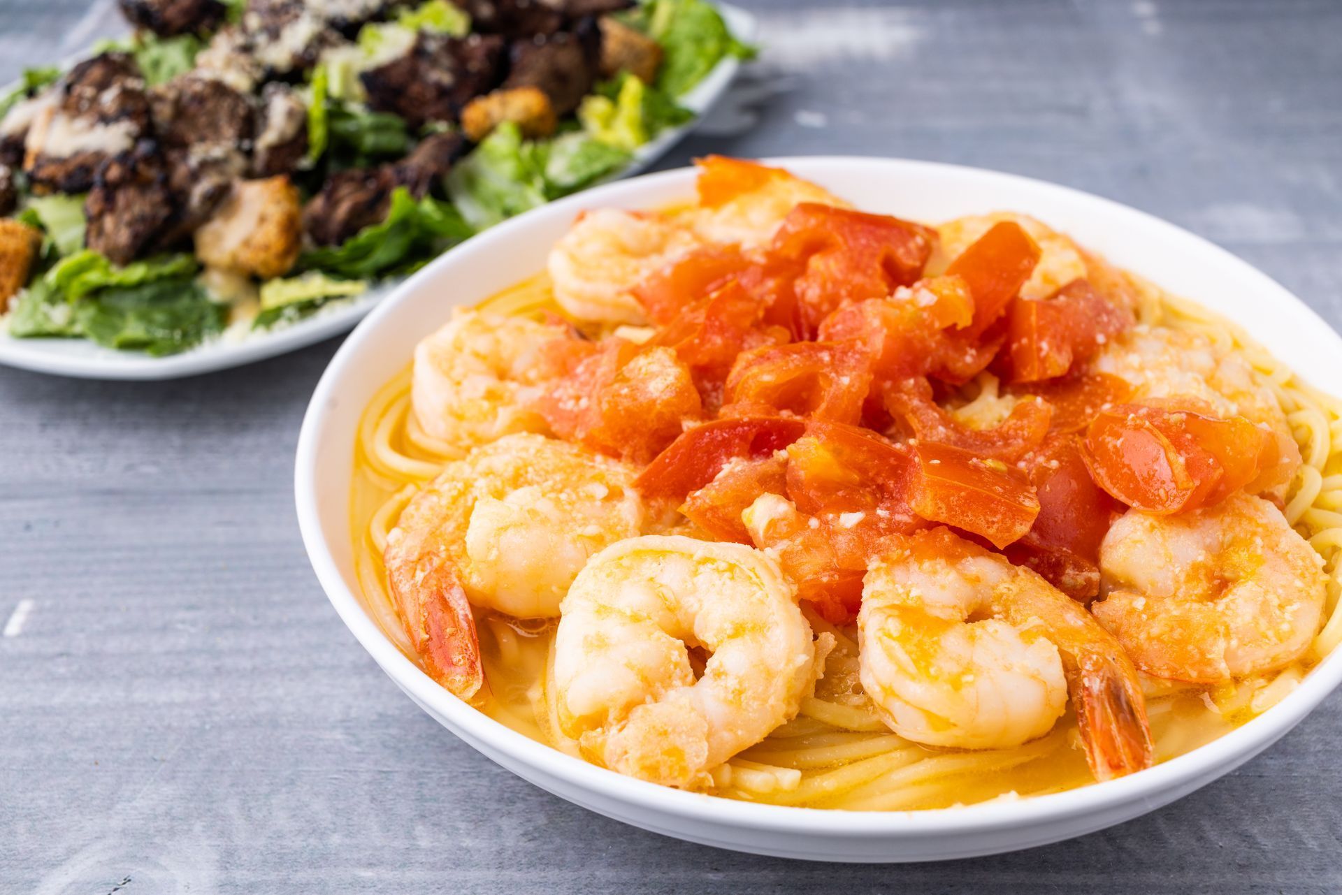 A bowl of shrimp and noodles with tomato sauce next to a plate of food.