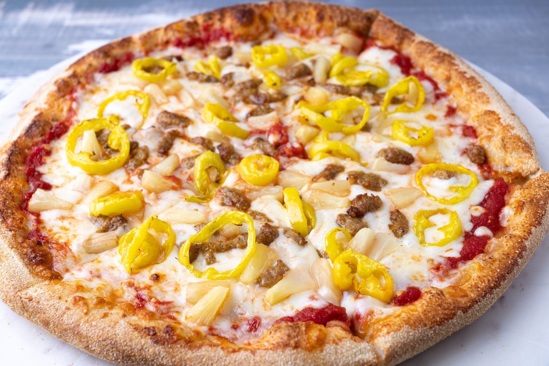A pizza with pineapple , sausage , peppers and cheese on a white plate.