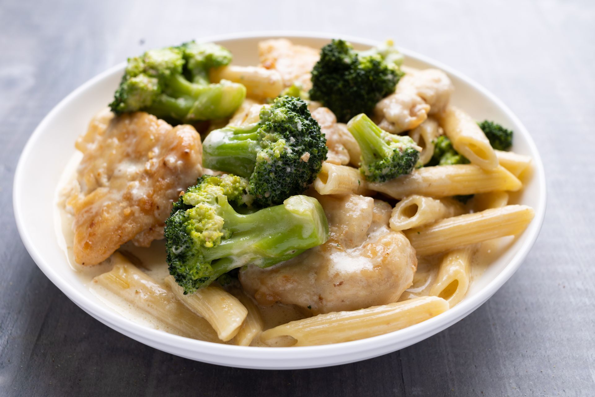 A white bowl filled with pasta , broccoli and chicken.