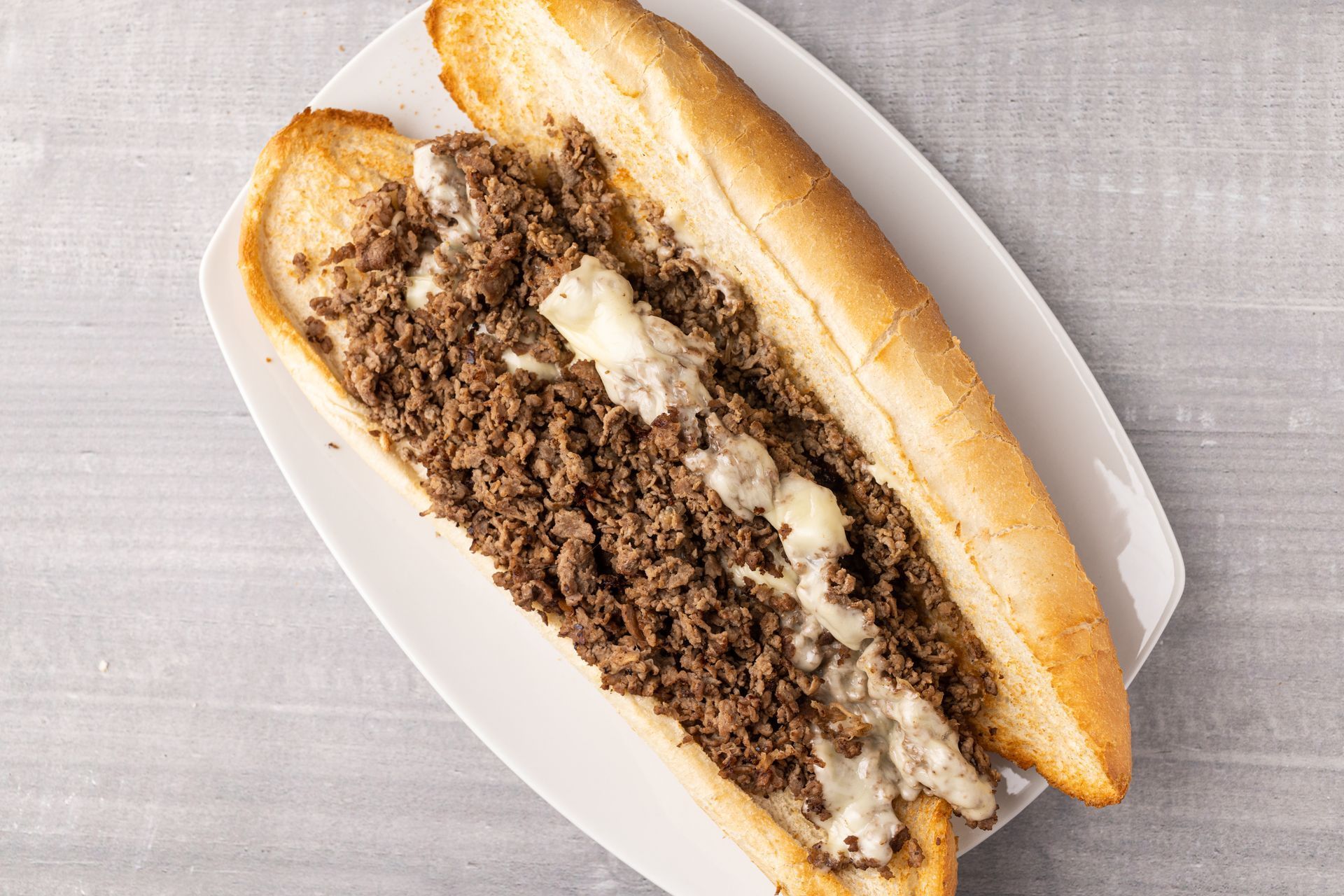 A steak sandwich with cheese on a white plate on a table.