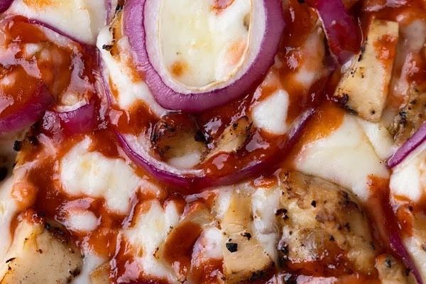 A close up of a pizza with chicken , onions and cheese.