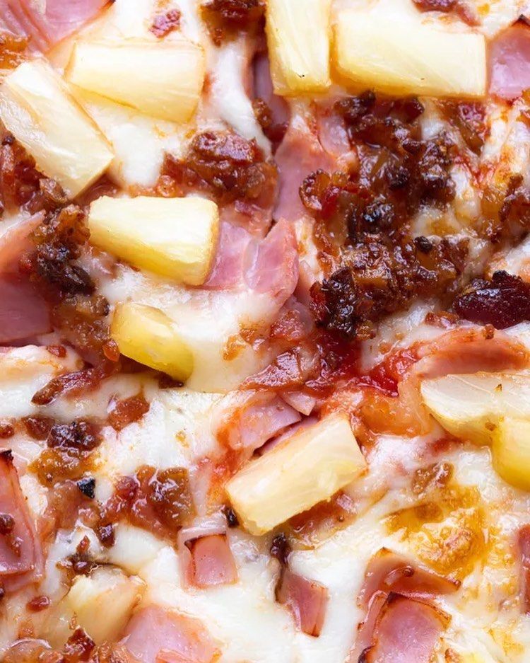 A close up of a pizza with pineapple , bacon and cheese.