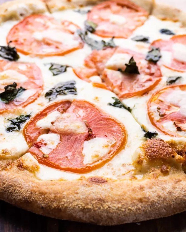 A close up of a pizza with tomatoes and cheese on a wooden table.