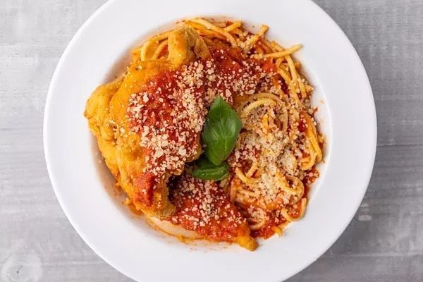 A white plate topped with spaghetti and chicken in tomato sauce.