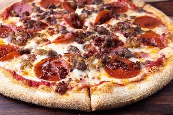 A pizza with pepperoni , sausage , bacon and cheese on a wooden table.