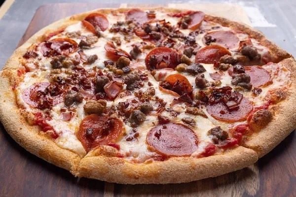 A pizza with pepperoni and sausage on it is sitting on a wooden table.