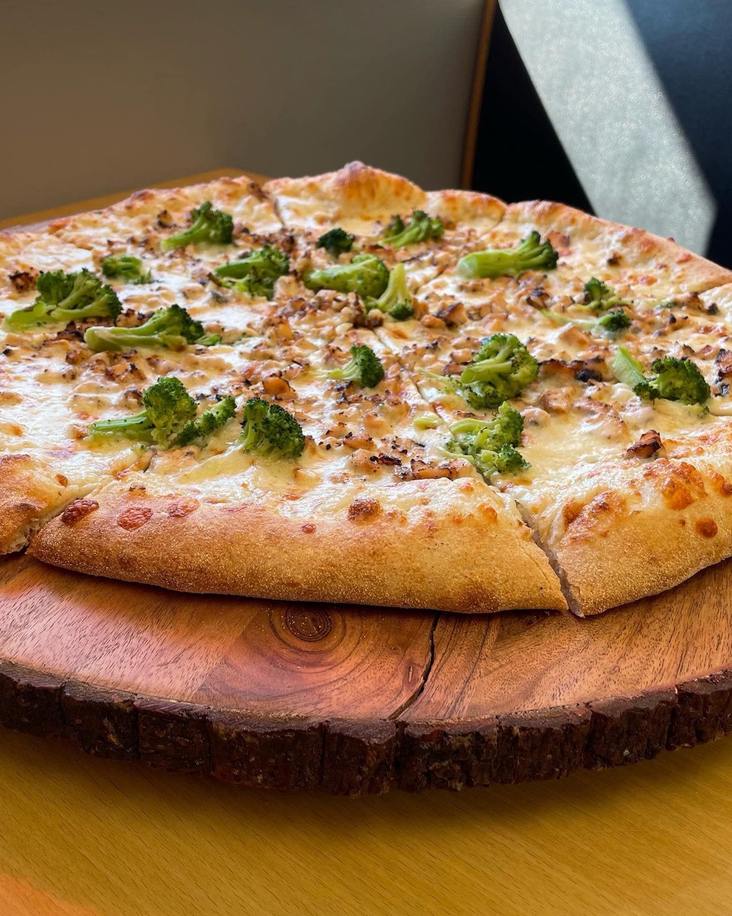 A pizza with broccoli and sausage is sitting on a wooden cutting board.