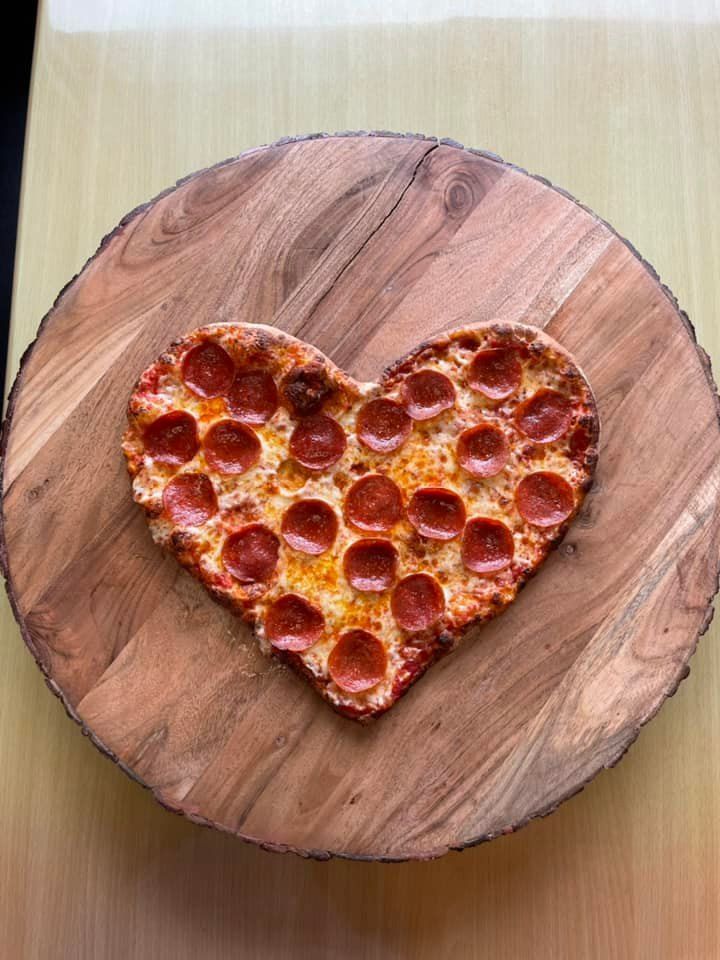A heart shaped pepperoni pizza is on a wooden cutting board.