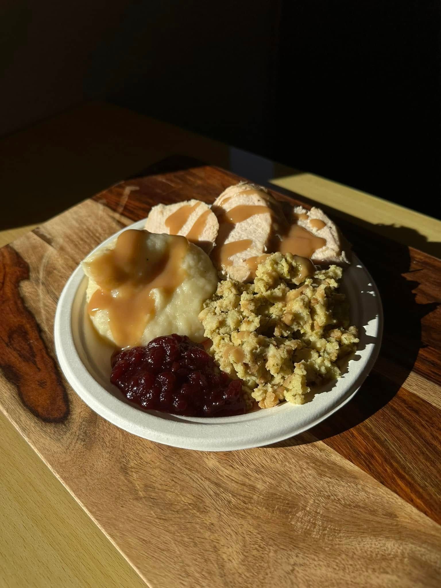 A plate of food with turkey , mashed potatoes , gravy and cranberry sauce on a wooden table.