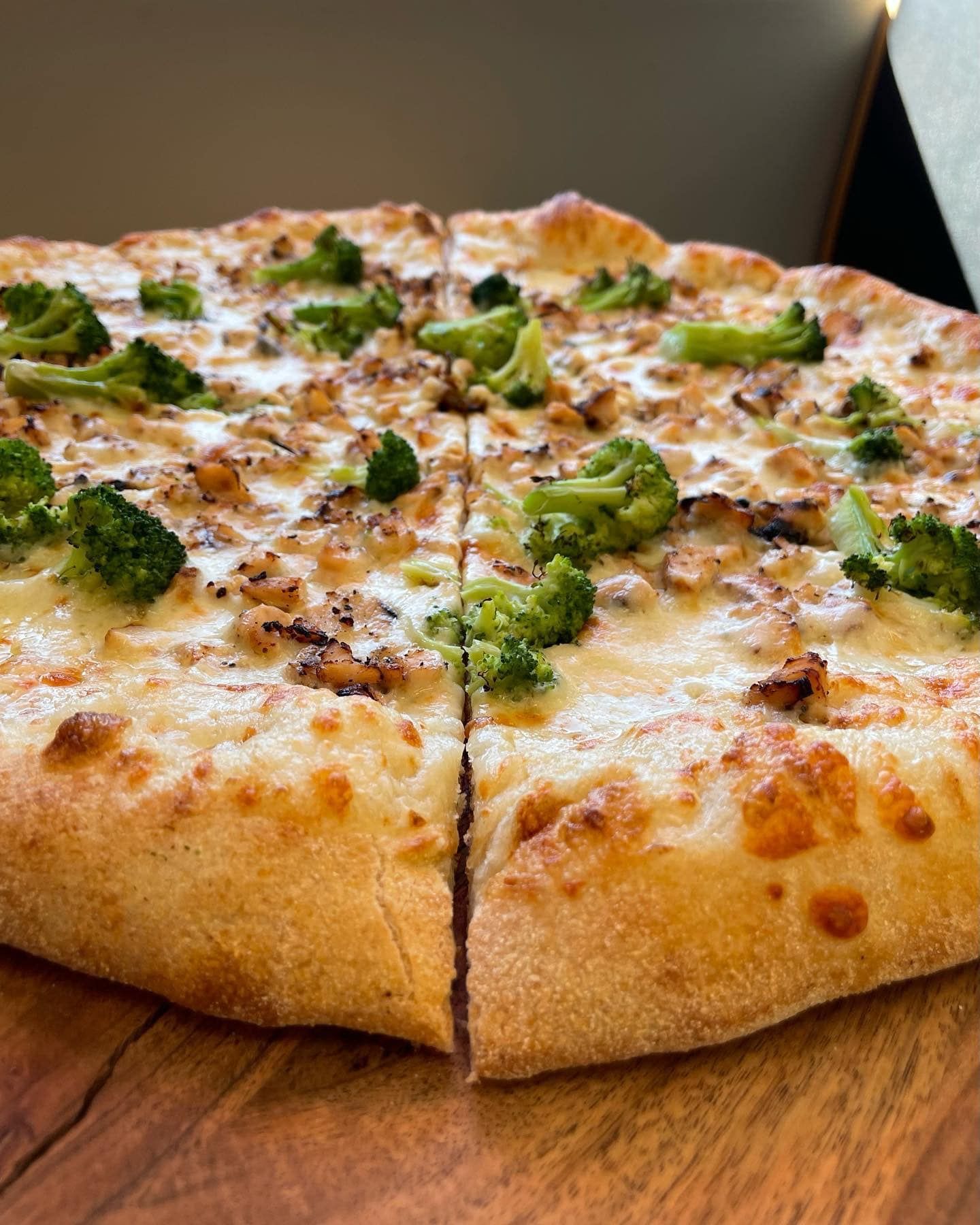 A pizza with broccoli and cheese is sitting on a wooden cutting board.