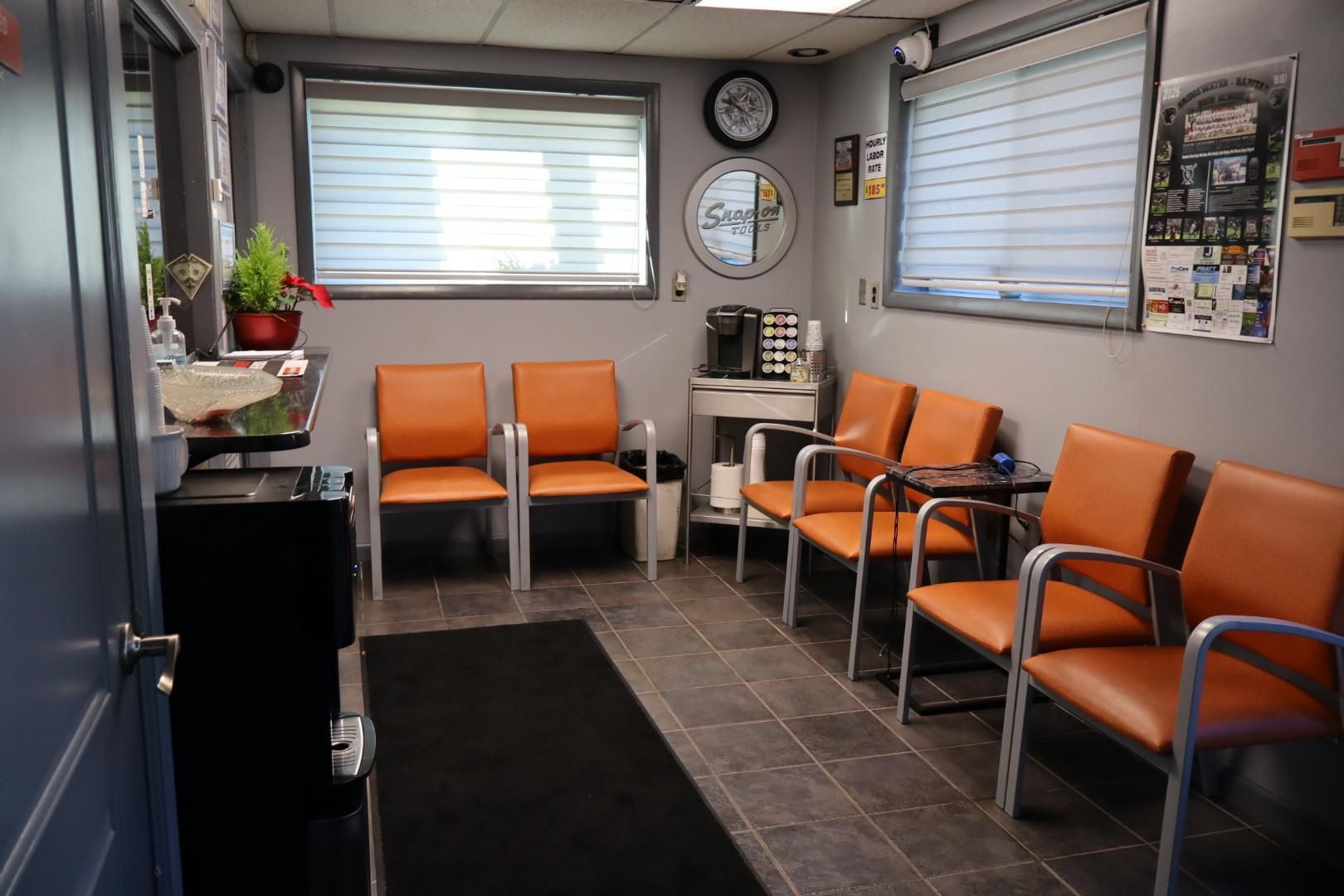 Small waiting room with orange chairs, wall clock, windows, and tiled floor