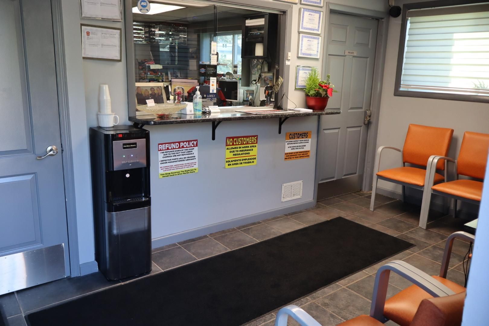 Waiting room with reception window, black floor mat, orange chairs, and water cooler.