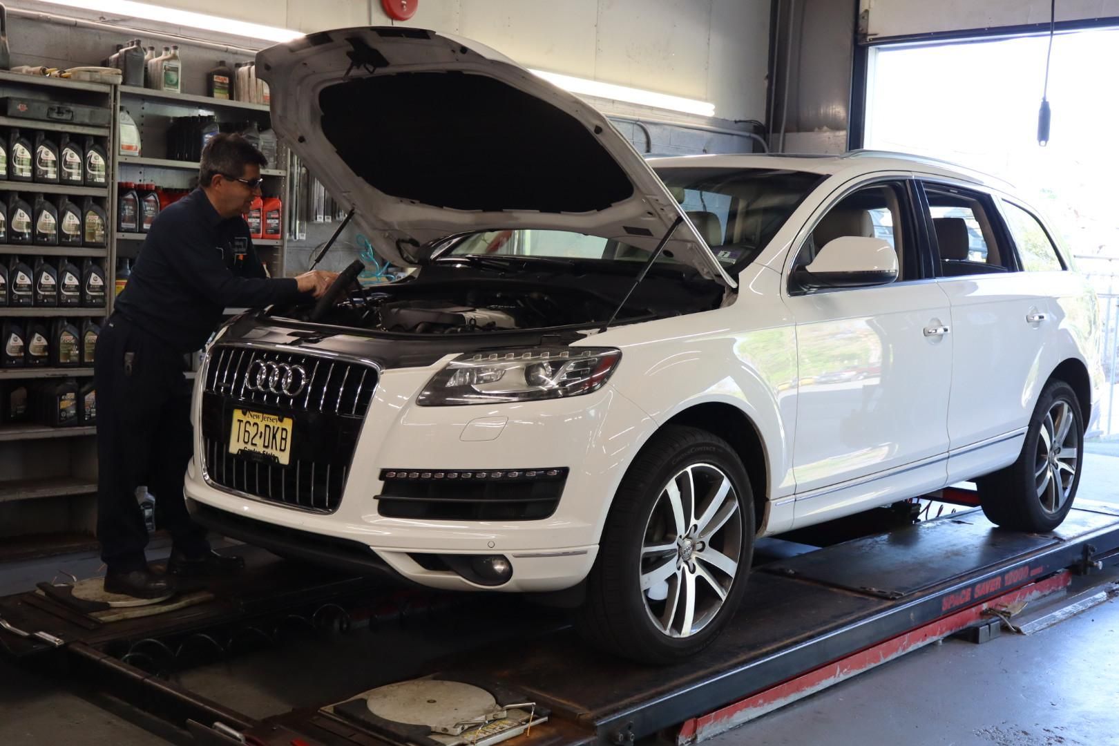 White SUV with hood open on a service lift while a mechanic works in an auto shop
