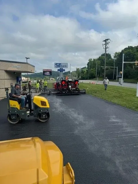 Asphalt paving in progress: Workers, machinery, and a new black surface outside a commercial building.