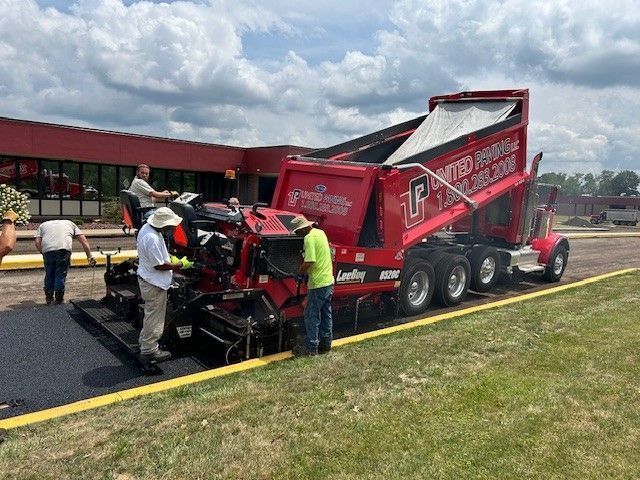 Asphalt paving operation with red truck and paver. Workers in safety vests.