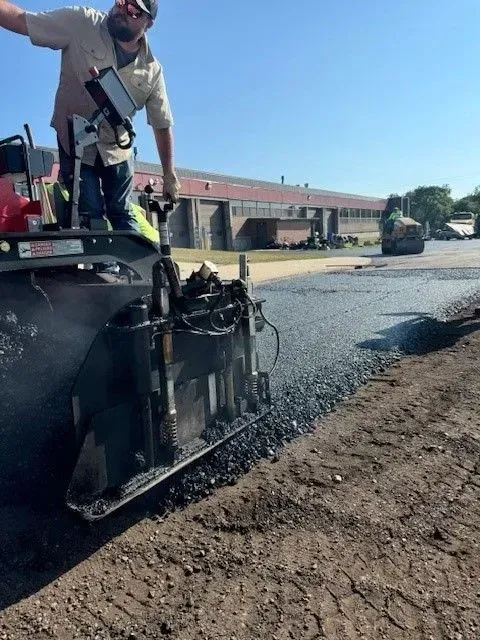 Person operating asphalt paving machine on a sunny day.