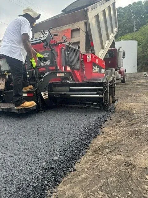 Man operating asphalt paving machine as dump truck unloads.