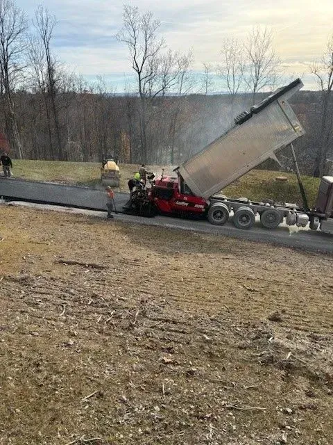 A dump truck unloading asphalt onto a newly paved road. Workers stand nearby.
