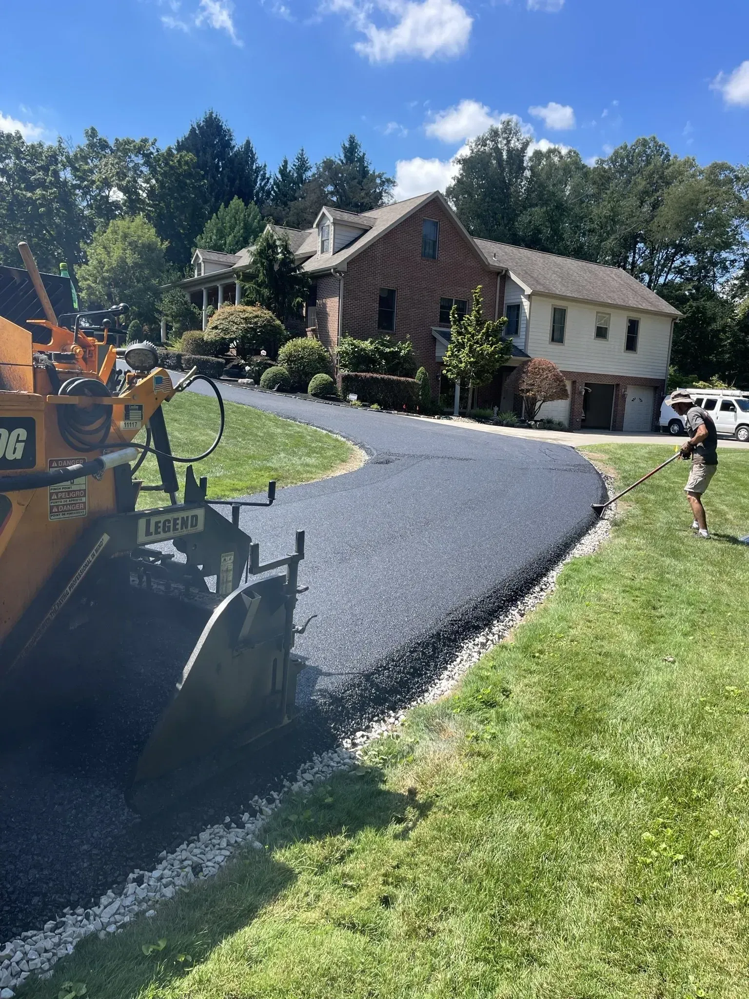 Asphalt paving a curved driveway in front of a house, a person watches.