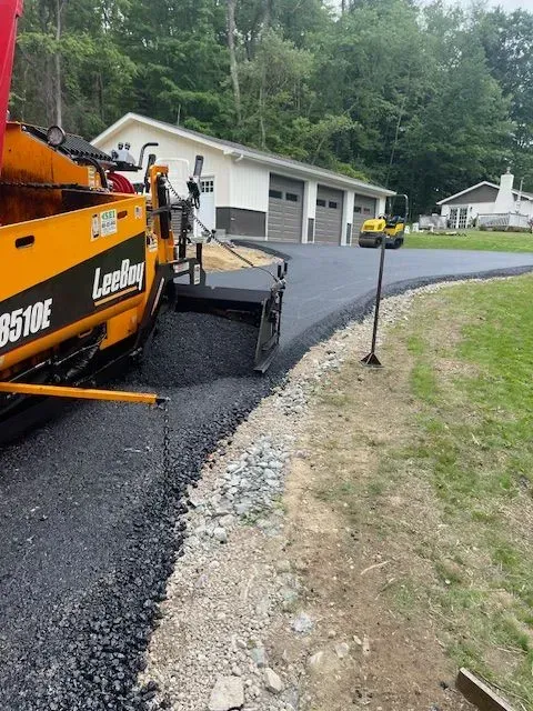Asphalt paving machine laying black asphalt on a driveway.