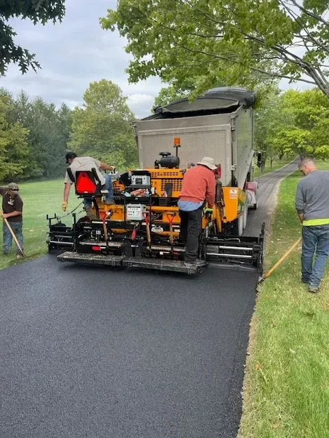 Paving crew laying asphalt on a road. Workers use machinery with a dump truck on an overcast day.