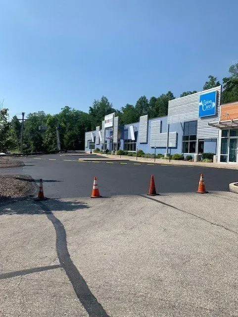 Freshly paved parking lot in front of a blue and white commercial building, with orange traffic cones.