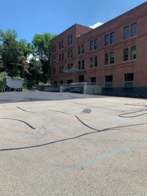 Brick building with many windows and a concrete area in the foreground. Blue sky.
