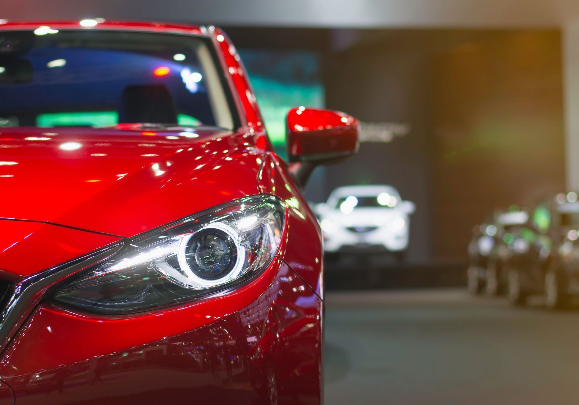 Close-up of a red sports car headlight in a parking garage, with other cars blurred in the background