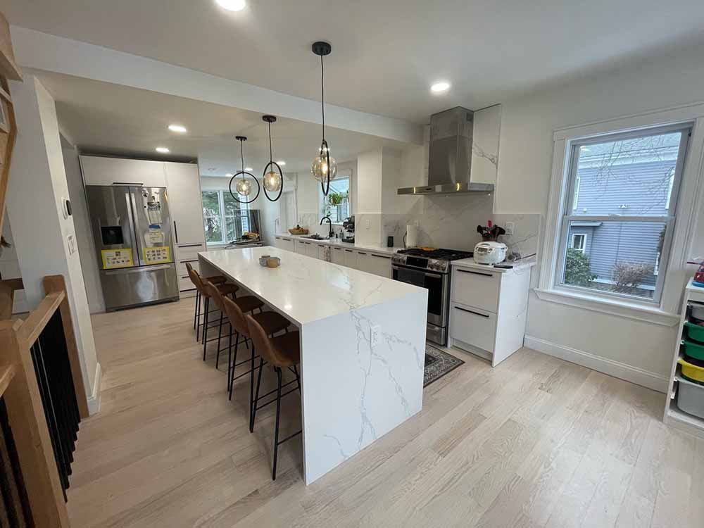 A kitchen with a large island , stools , a refrigerator and a stove.
