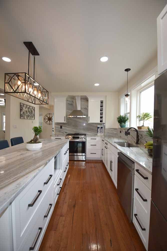 A kitchen with white cabinets , hardwood floors , stainless steel appliances and a large island.