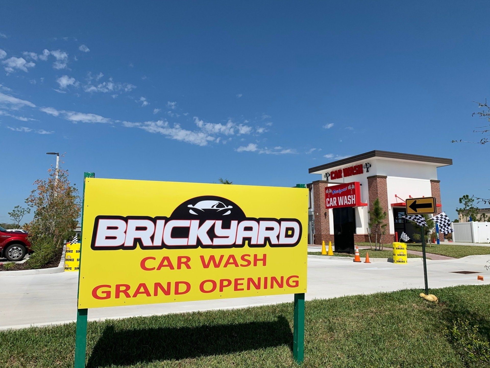 Yellow sign for Brickyard Car Wash grand opening. Building behind sign with a red brick facade.