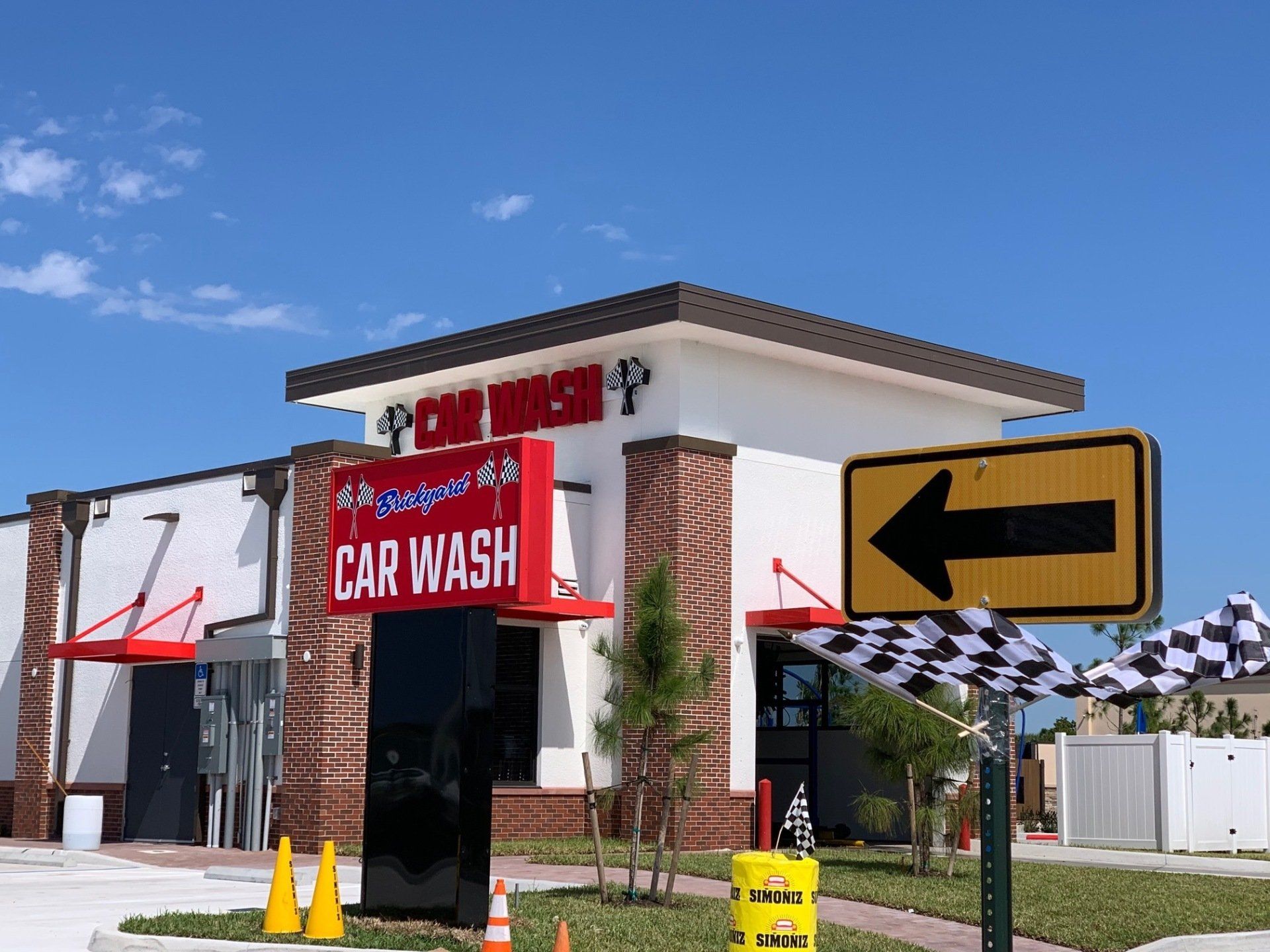 Car wash building with a sign, direction arrow, and checkered flags under a blue sky.