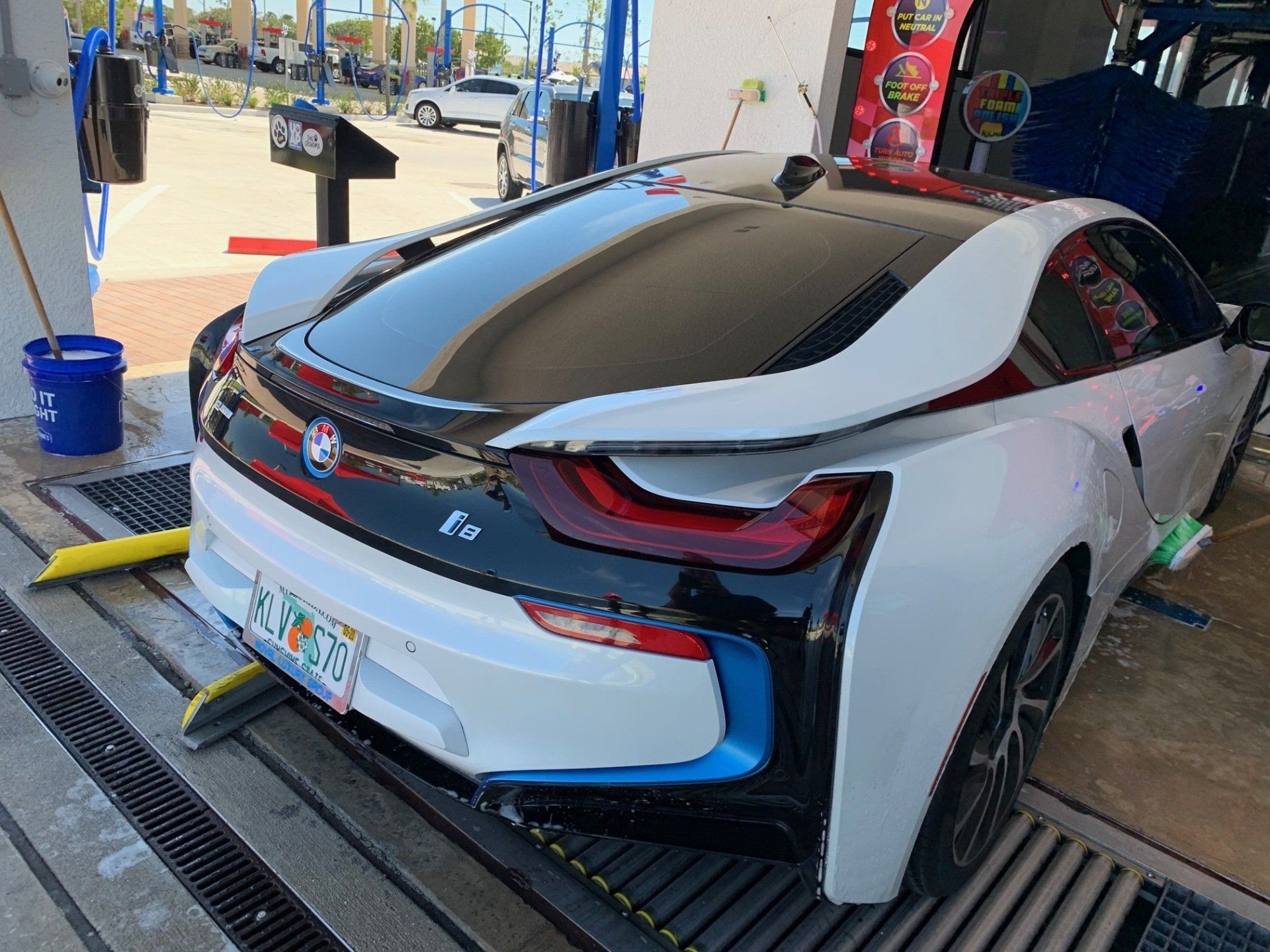 White BMW i8 at a car wash, with black accents and blue trim.