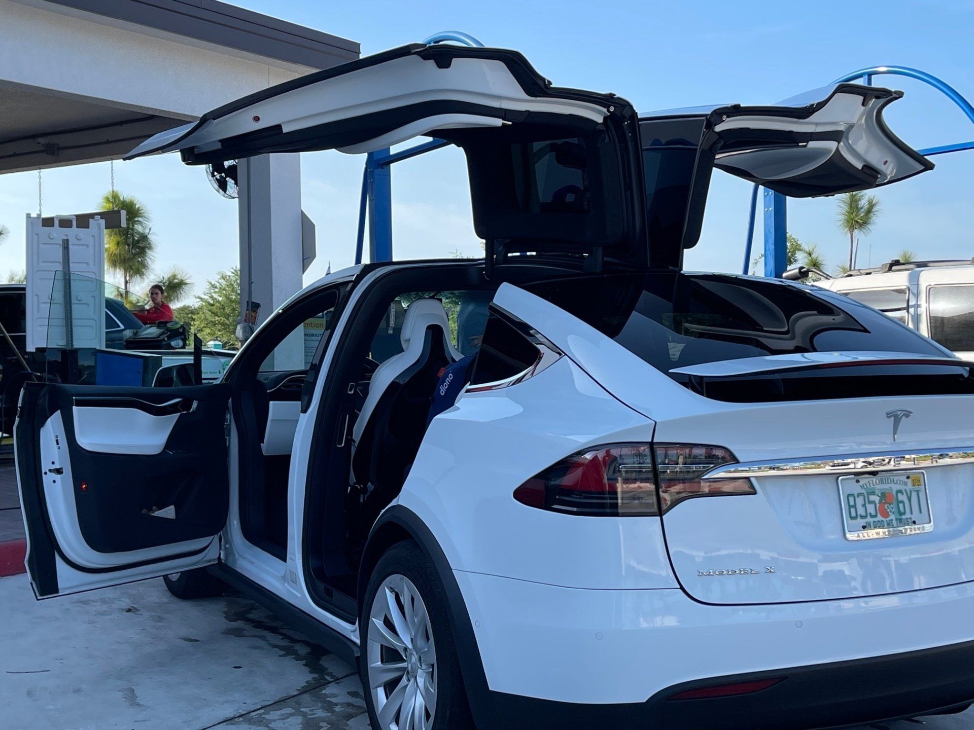 White Tesla Model X with falcon-wing doors open at a car wash.