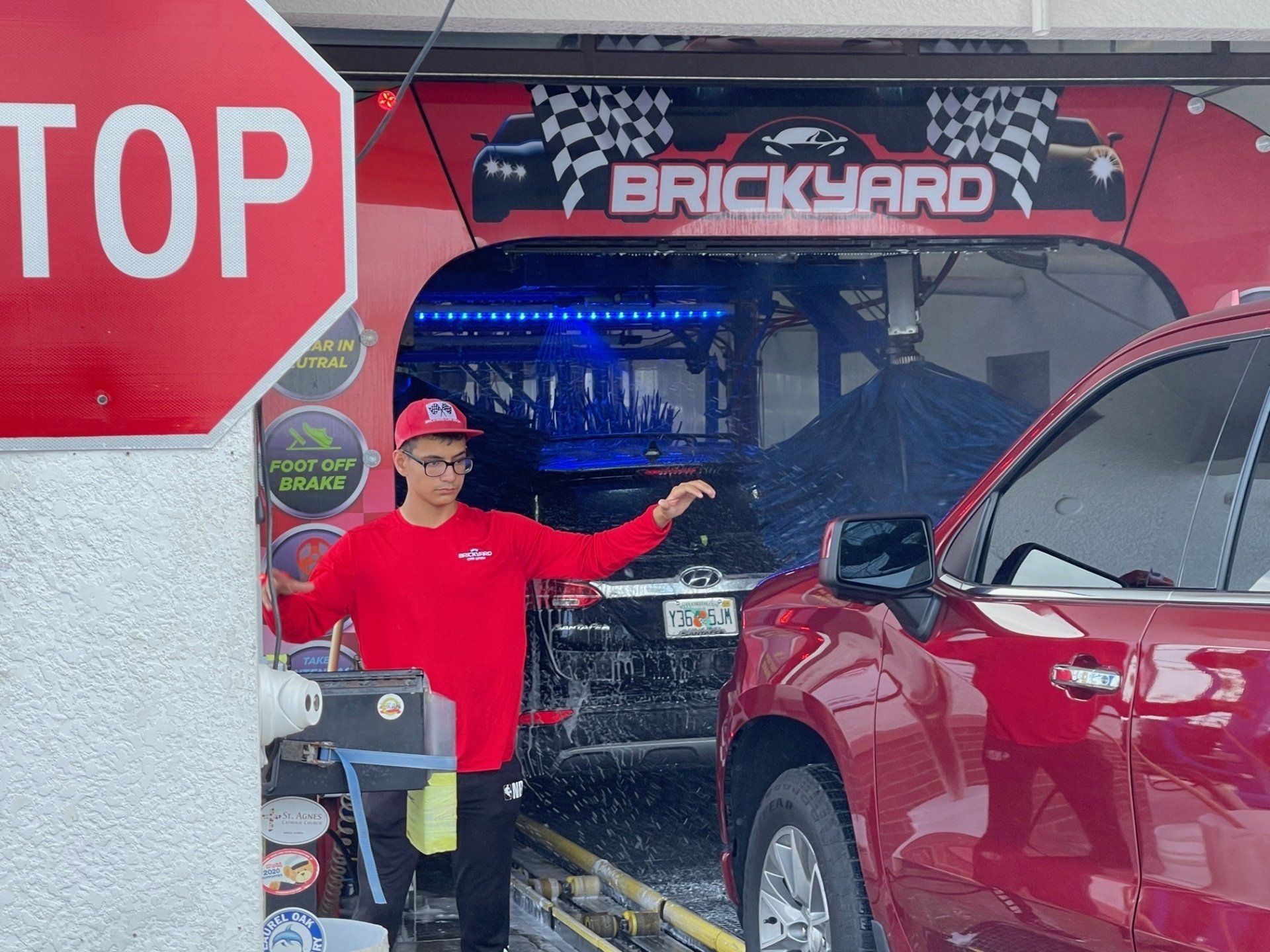 Man in red directs a red SUV at Brickyard car wash. Stop sign visible.