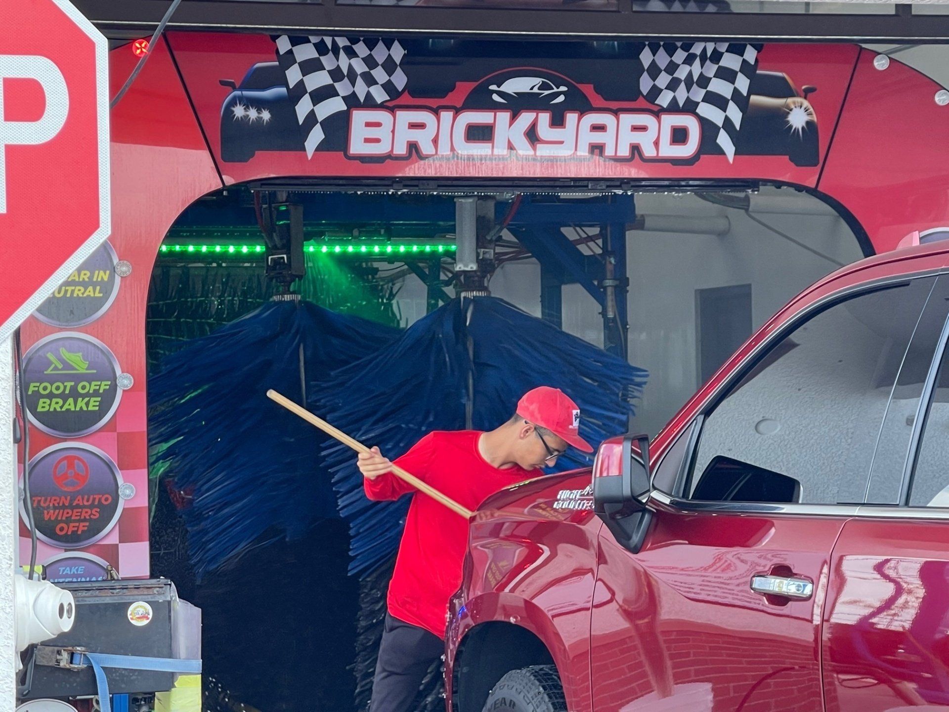 Man in red uniform preps a red car for a car wash at the Brickyard car wash.
