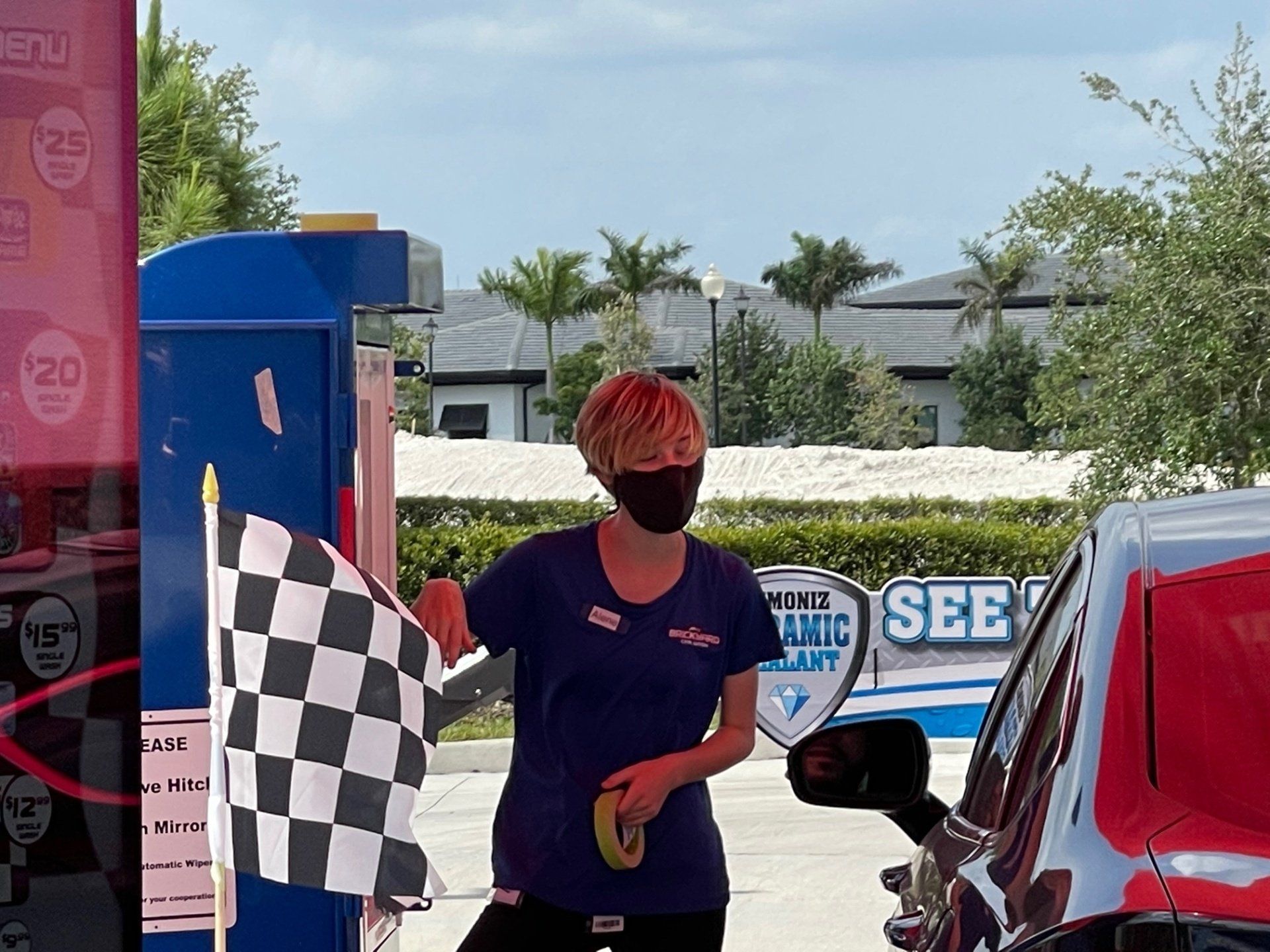 Woman in mask waves checkered flag at car wash.