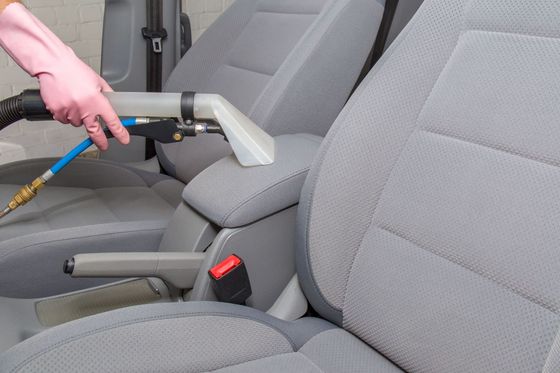 Hand in pink glove cleans gray car seat with a professional steam vacuum.