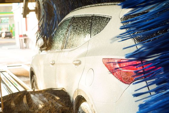 Car in a carwash, covered in white soap. Blue brushes and water spray the vehicle.