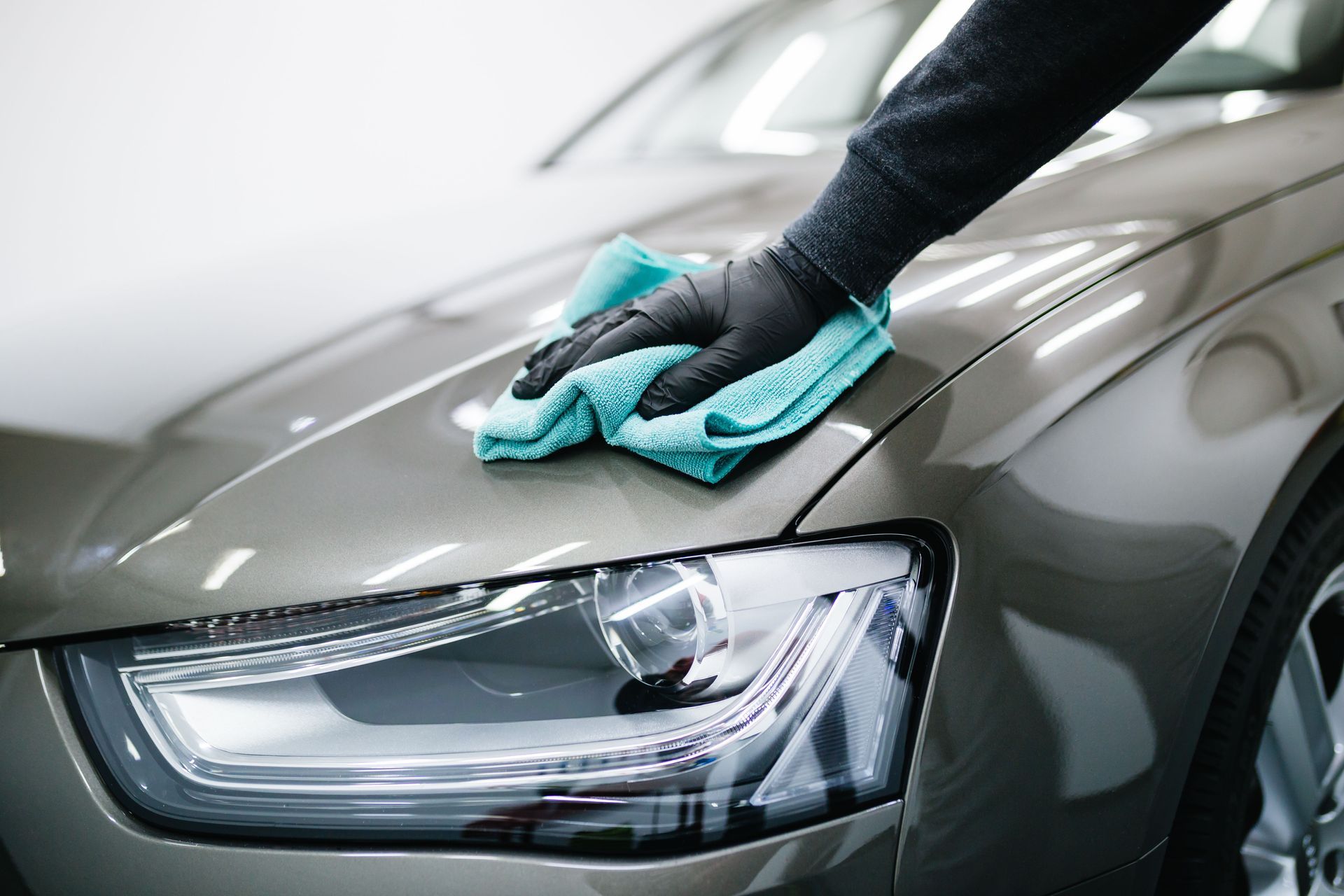Hand wearing black glove wiping the hood of a car with a blue cloth.