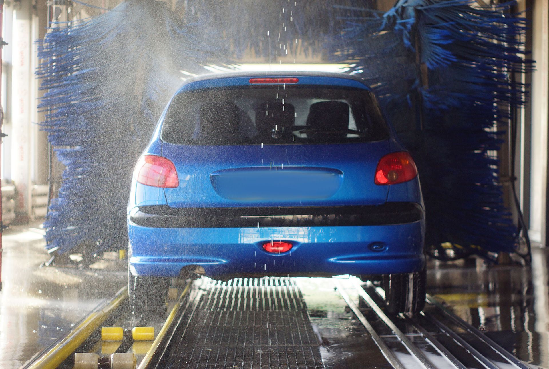 Blue car being washed in an automated car wash, with water and rotating brushes.