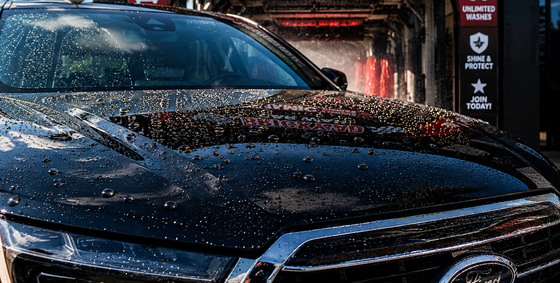 Black car hood covered in rain droplets outside a car wash