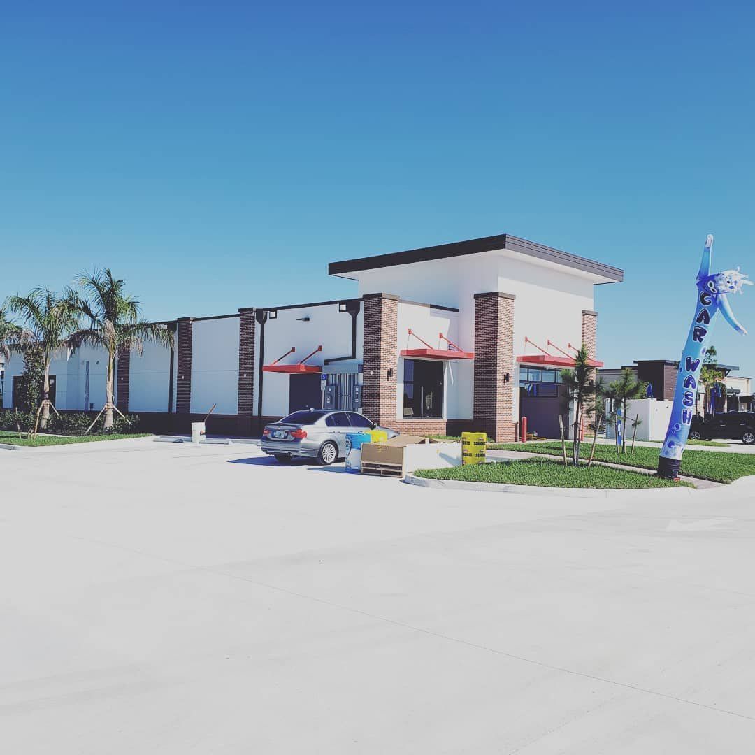 A car wash with a white and red building, blue sky, and a blue air dancer.