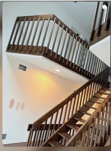 Wooden staircase with railing in a home, ascending towards a balcony with matching railing.