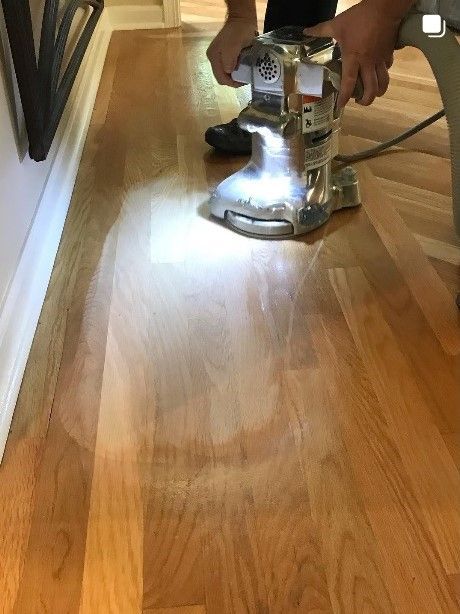 A person is sanding a wooden floor with a machine.